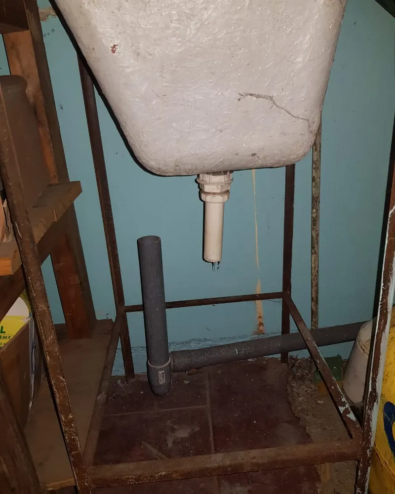 Lavadero de cemento sobre una estructura metálica, con su desagüe y una tubería antigua a la vista