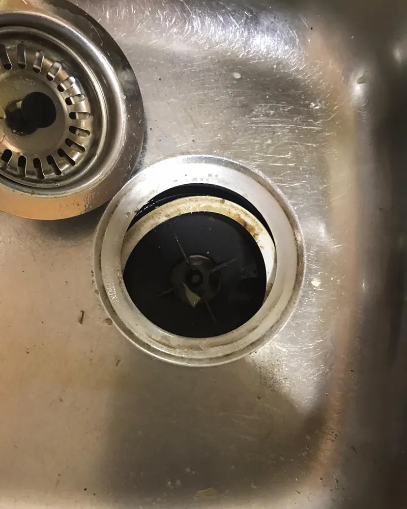 Desagüe de un lavaplatos de acero inoxidable visto desde arriba, con la canastilla retirada