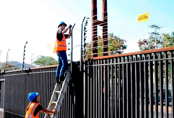 Técnicos instalando un cerco eléctrico sobre una reja con escalera