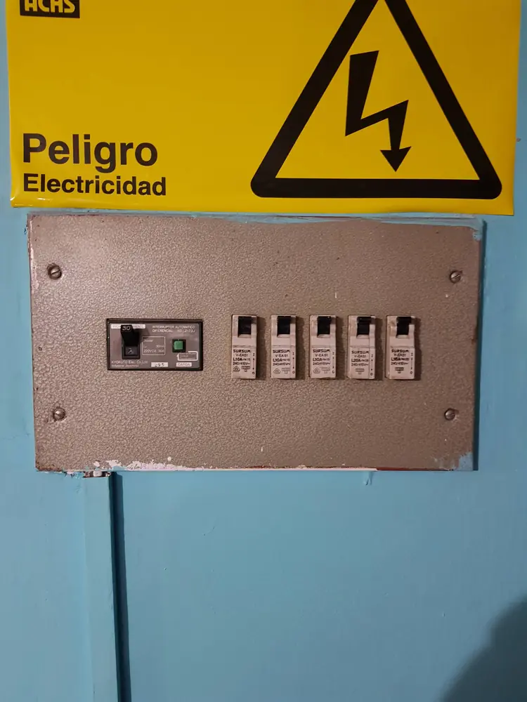Tablero antiguo de tapones bajo un letrero de peligro electricidad