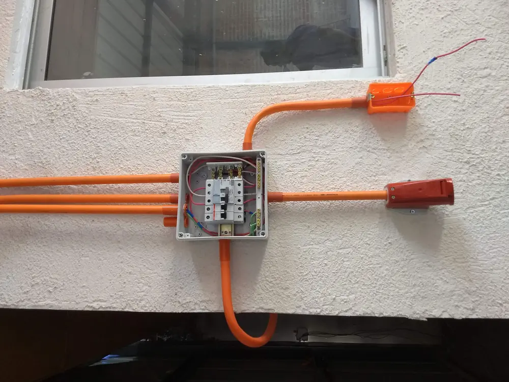 Canalización exterior con tubo naranjo y caja de derivación en una fachada