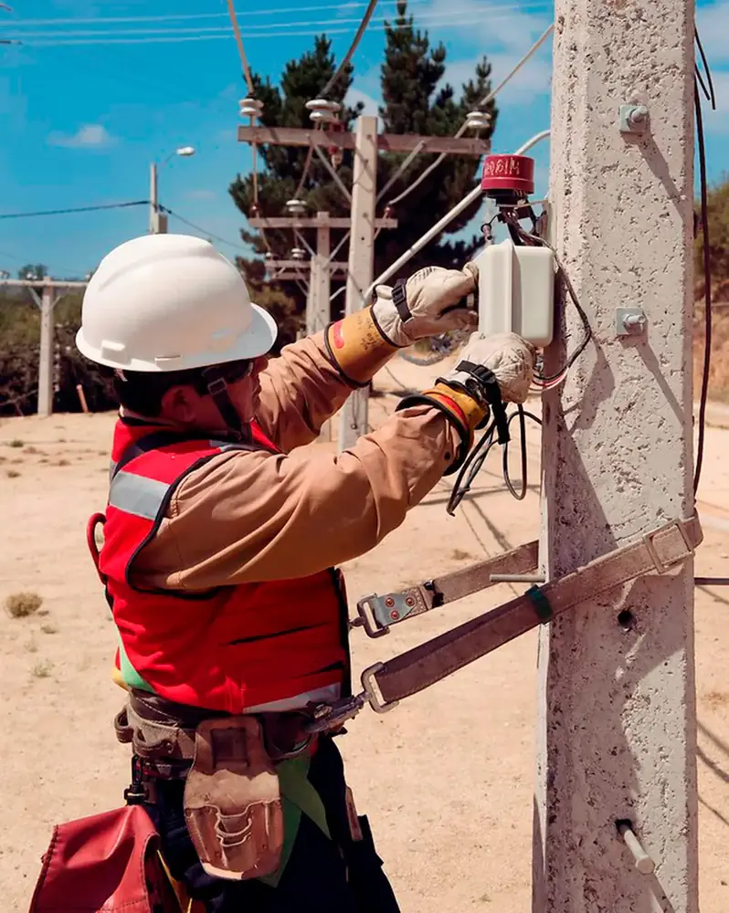 Técnico con casco y arnés trabajando en un medidor en un poste