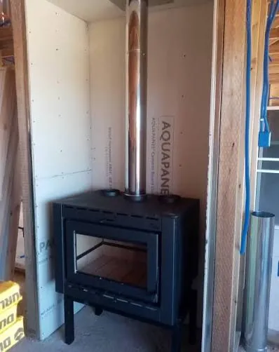 Estufa a leña instalada en una casa en construcción, con placas incombustibles en los muros