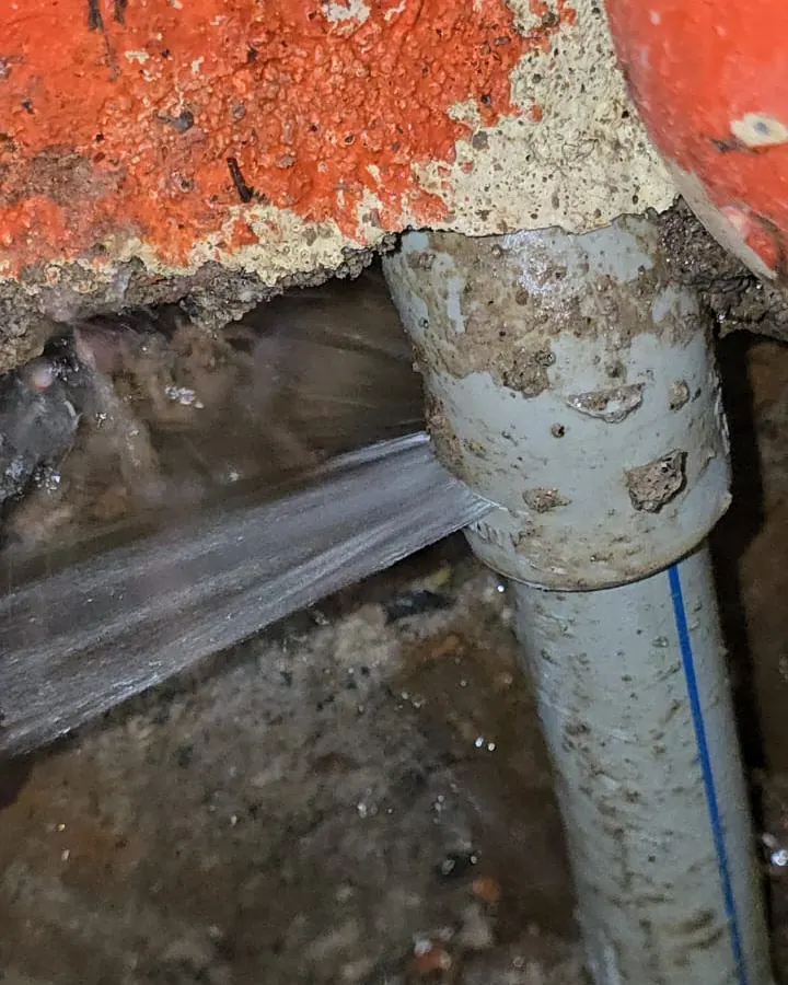 Chorro de agua saliendo de una cañería junto a la base de un muro pintado de rojo