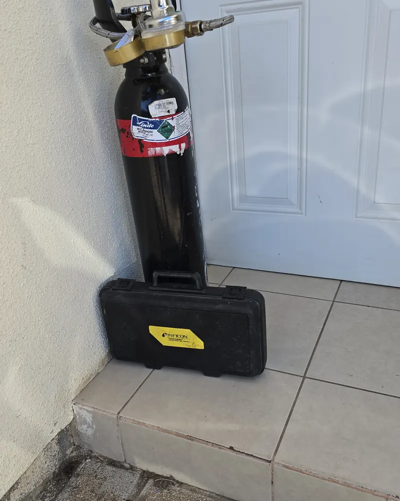 Cilindro de gas trazador y maletín del detector en el piso de un pasillo