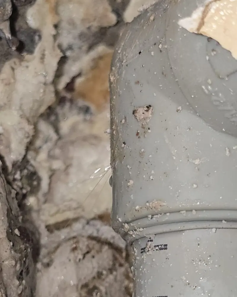 Codo de cañería gris con hilos de agua muy finos saliendo de la unión