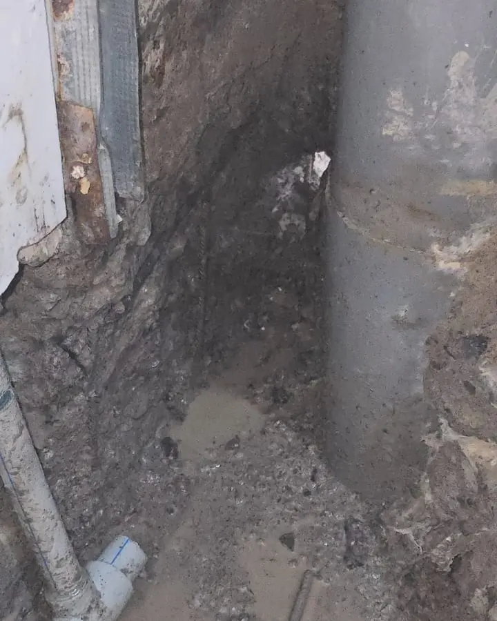 Excavación bajo el piso con agua acumulada y tierra húmeda junto al muro