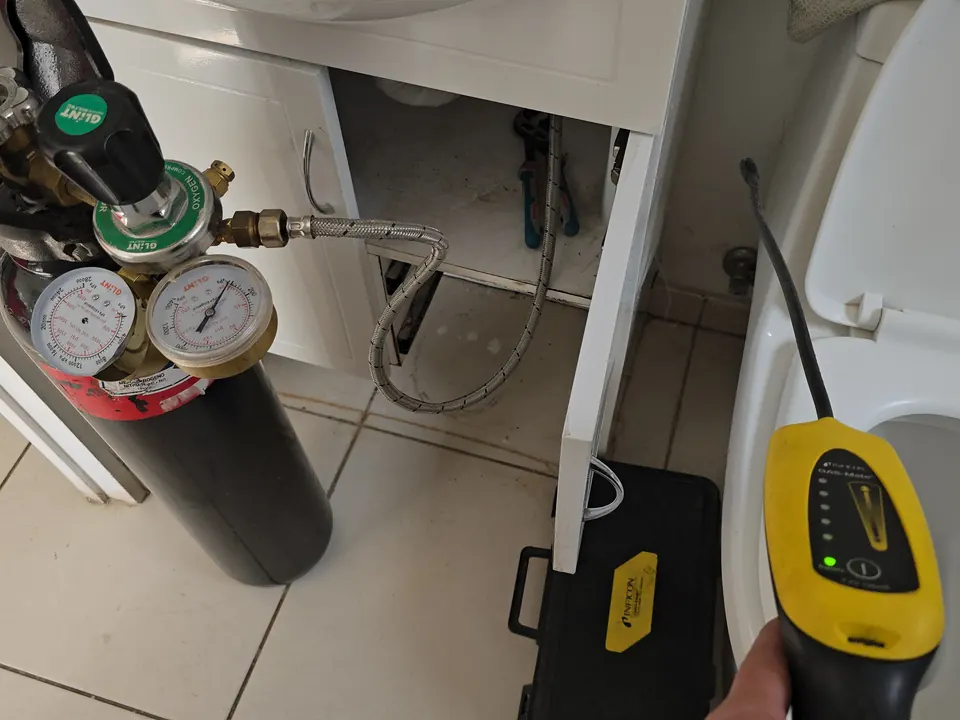 Cilindro de gas trazador con regulador y manómetros conectado a la red de agua de un baño, junto al detector amarillo