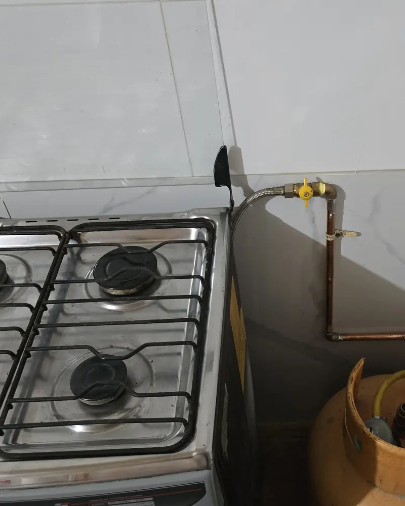 Cocina a gas de cuatro platos junto a un cilindro de gas licuado