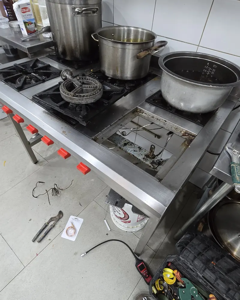 Cocina industrial de acero con ollas y herramientas en el suelo durante una reparación