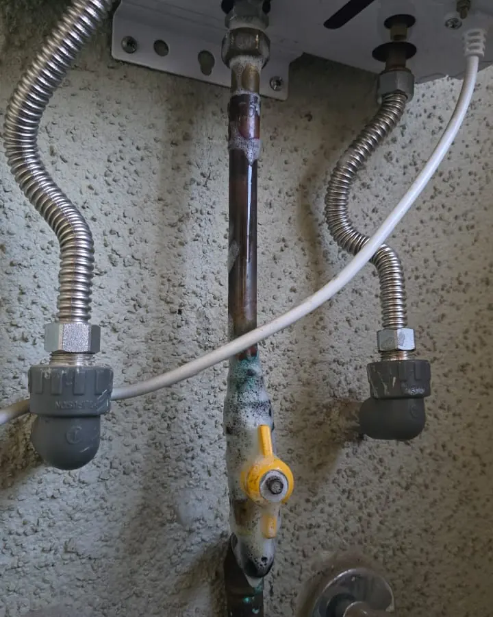 Conexiones de agua y gas bajo un calefont con una llave amarilla