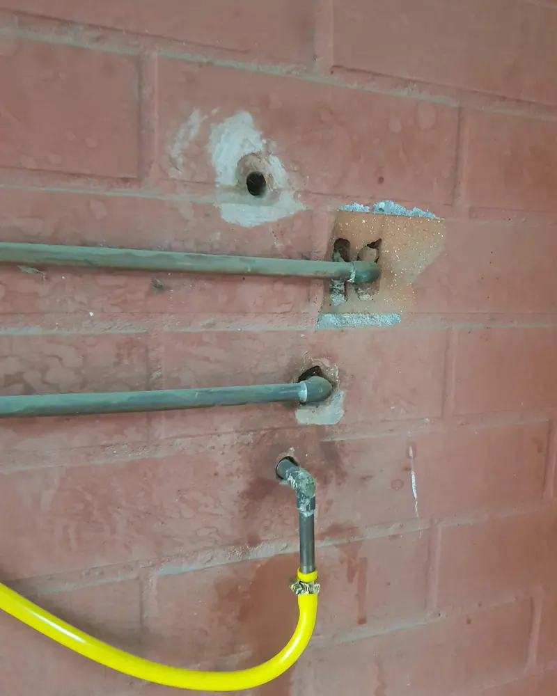 Cañería de gas de cobre fijada a un muro de ladrillo con un flexible amarillo