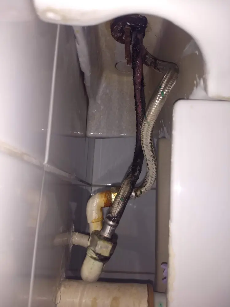 Flexible del WC corroído y oxidado bajo el estanque