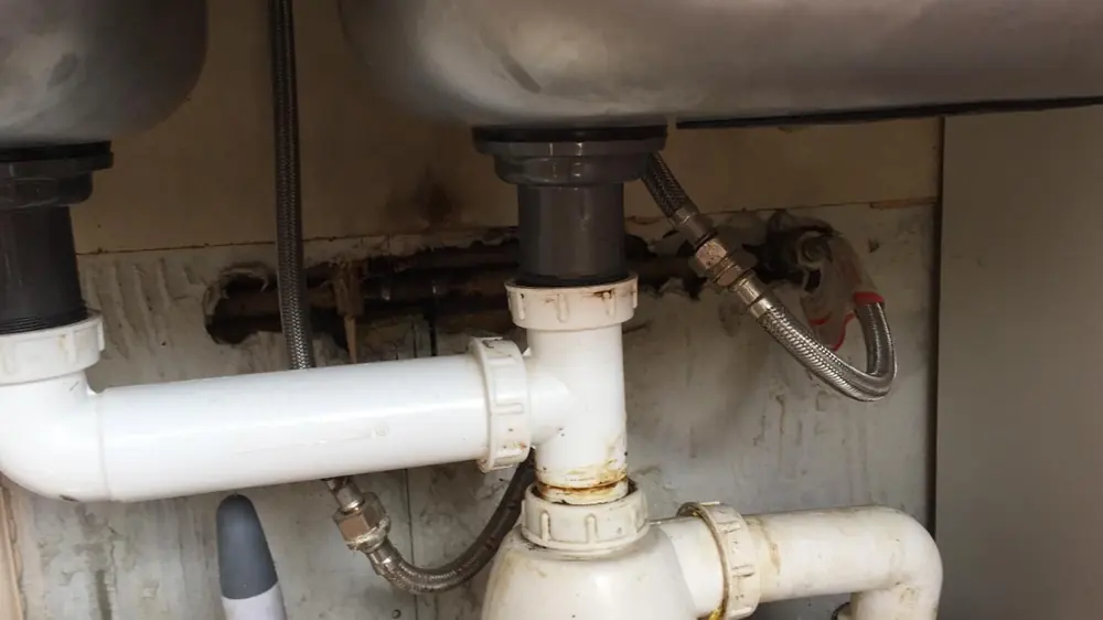 Sifón doble de PVC bajo un lavaplatos de dos bateas