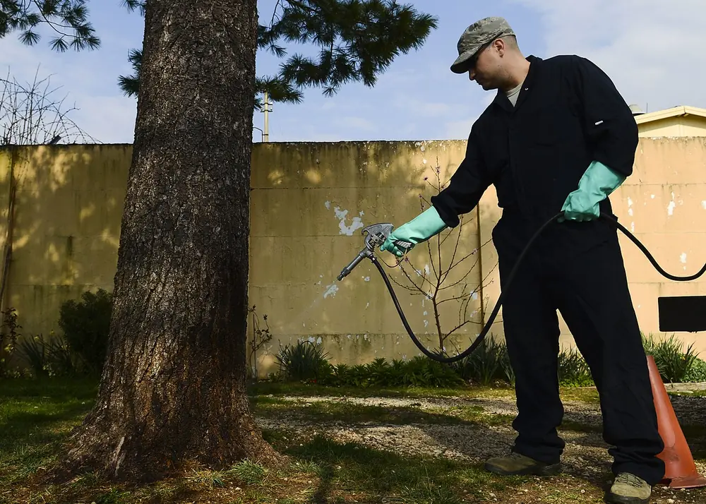 Técnico con guantes aplicando producto con una manguera en el perímetro de un jardín