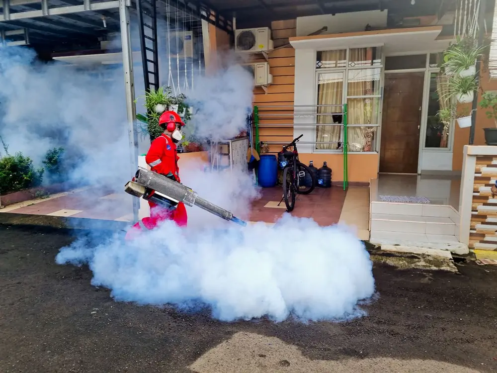 Técnico con casco rojo nebulizando frente a una casa