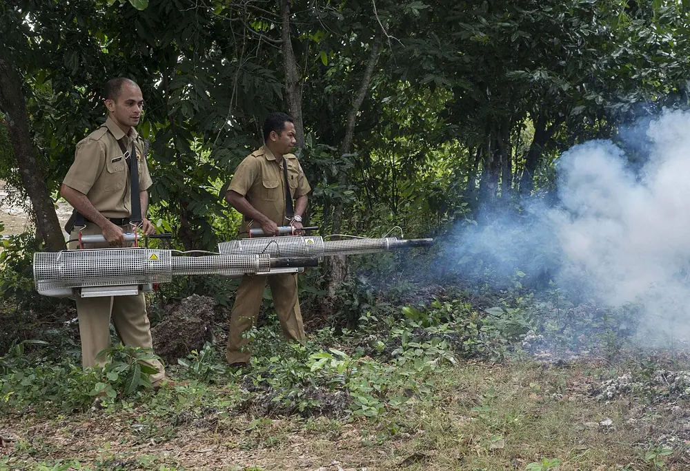 Dos técnicos con termonebulizadores en un sector con árboles