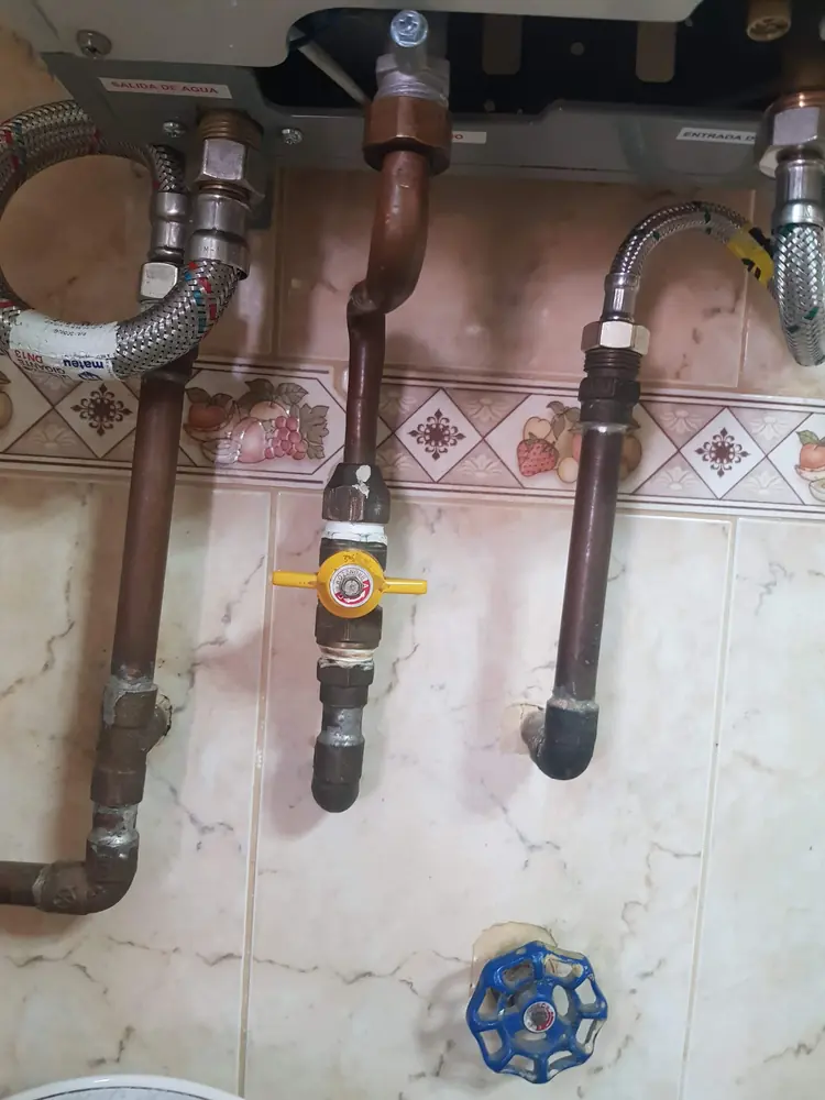 Red de cobre con llave de gas amarilla y flexibles bajo un calefont
