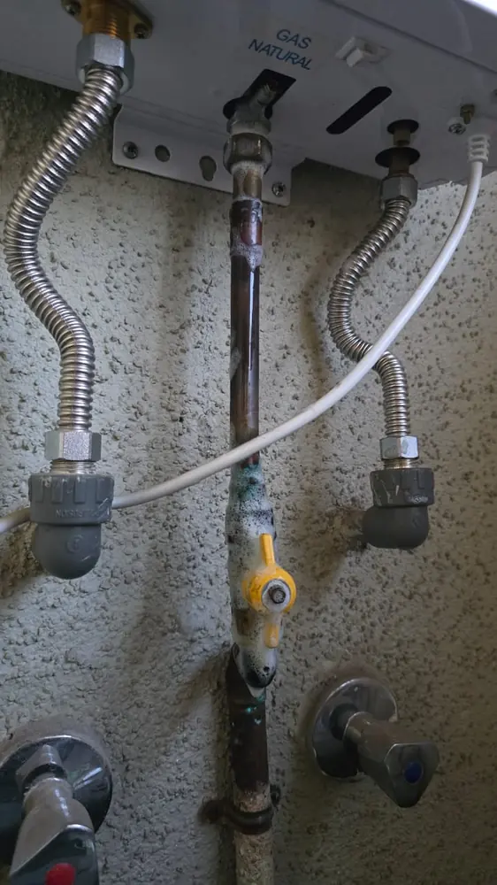 Cañería de cobre soldada con una llave de gas amarilla bajo un calefont