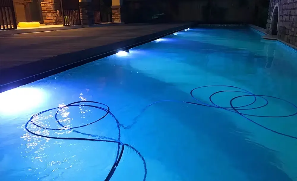 Piscina iluminada de noche con los cables de los focos sobre el agua durante el cambio